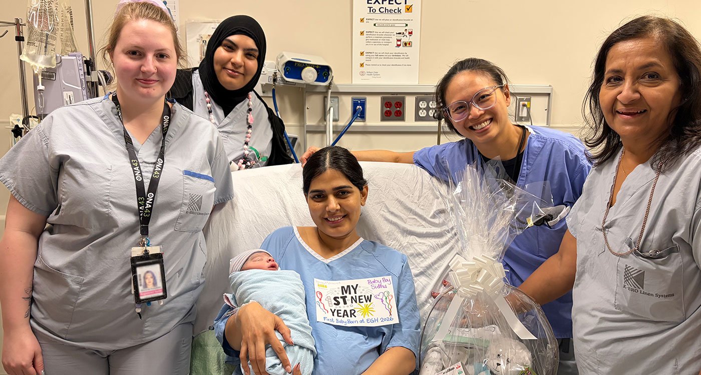 A group of hospital staff stand in a group around new parent holding a newborn in a hospital bed