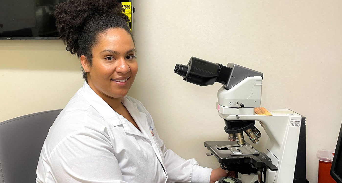 Samantha Baker, Medical Laboratory Technologist at Osler, poses in front of a microscope