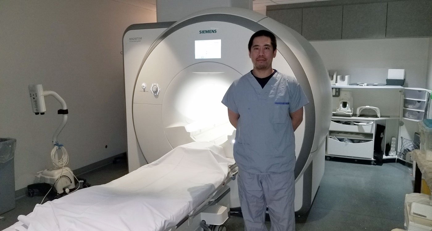 Vince Wong, MRI Technical Specialist at Osler, stands in front of a MRI machine
