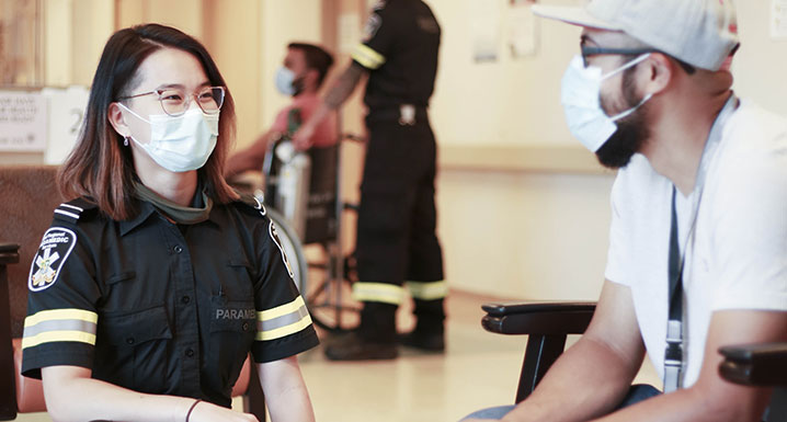 A paramedic kneels down to speak with a patient sitting on a chair