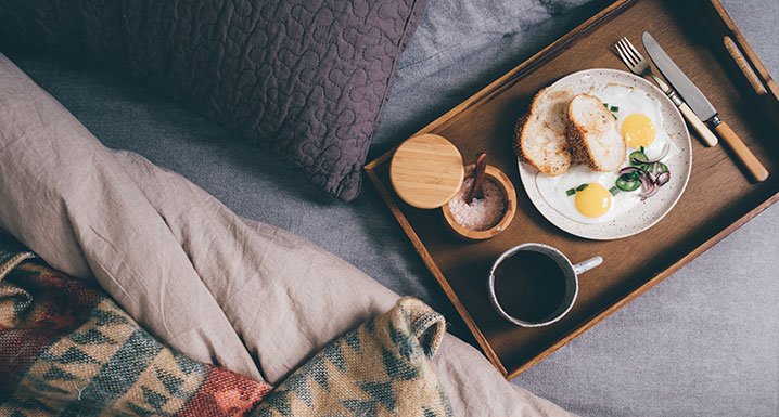 A tray of breakfast food and coffee on top of a bed