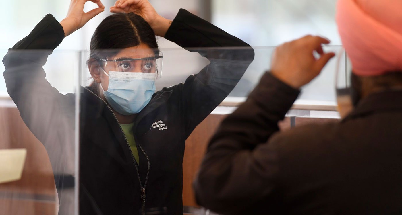 Staff member demonstrates to a patient on how to put on a mask