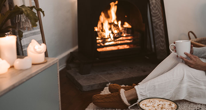 A person relaxing in front of a roaring fireplace with candles lit around the room