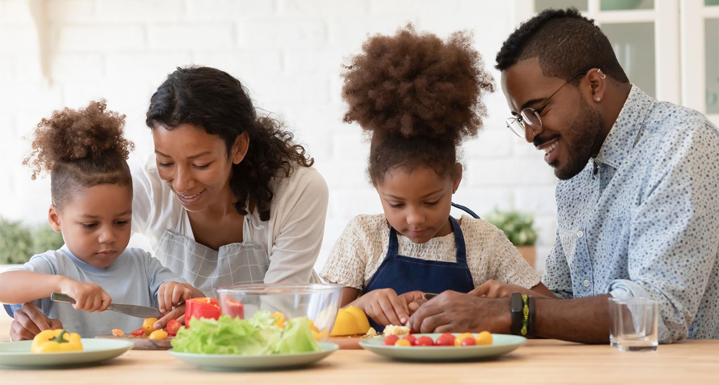 A mother and father help their son and daughter prepare a meal