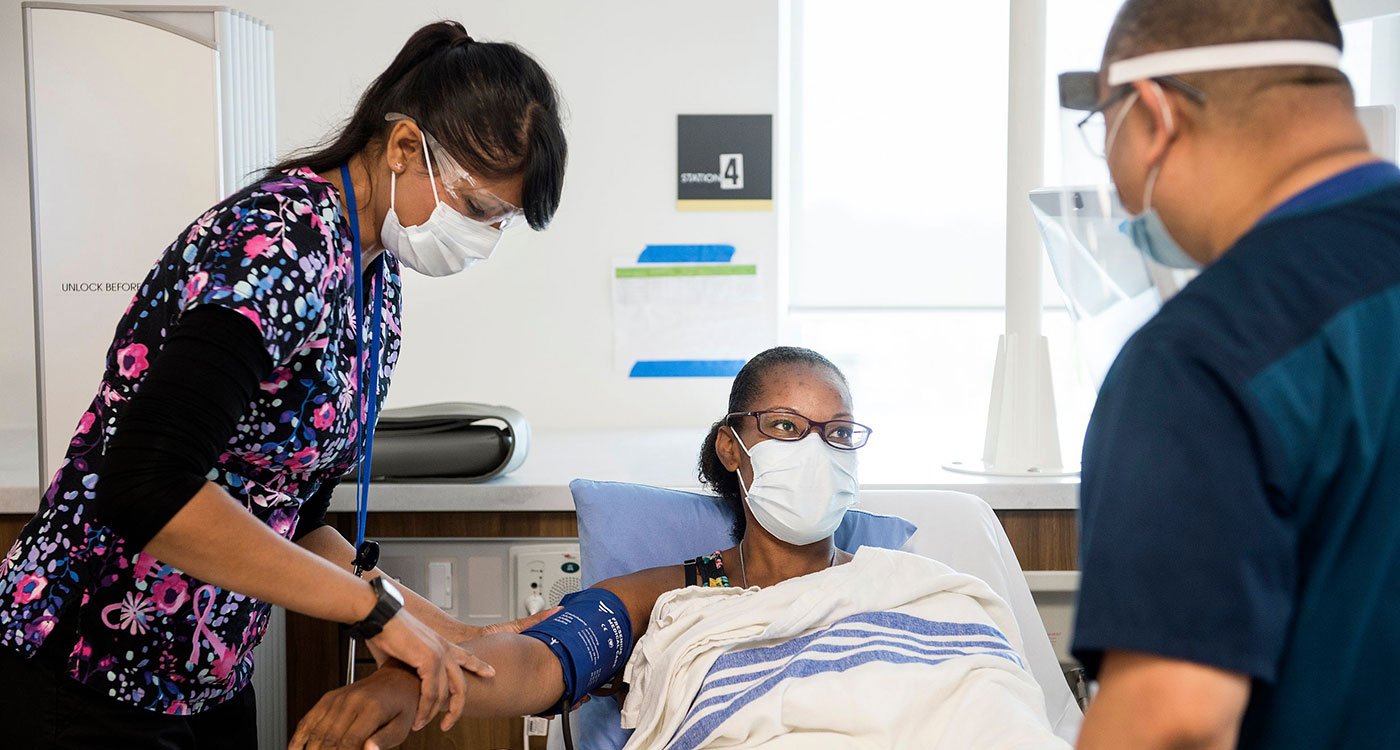 Two clinical staff members assist a patient with checking her heart rate.