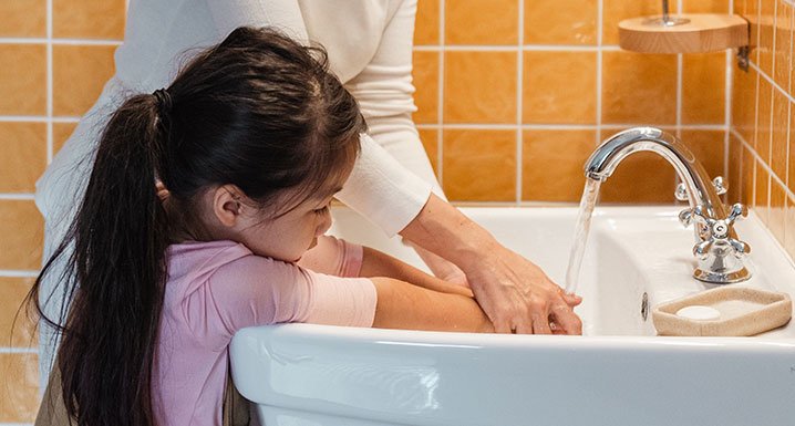 Mother helping her young daughter wash her hands